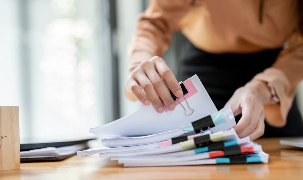 Woman hands working in Stacks of paper files for searching and checking unfinished divorce document 