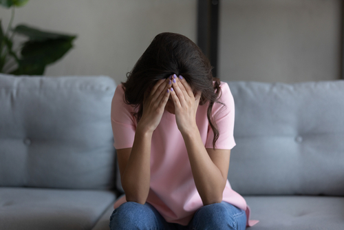 Upset woman sitting on a couch with her head in her hands, showing grief and emotional distress.