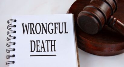 Close up of a notebook with the words wrongful death written on the page next to a wooden judge’s gavel on a white table.