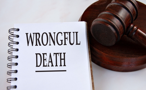 Close up of a notebook with the words wrongful death written on the page next to a wooden judge’s gavel on a white table.