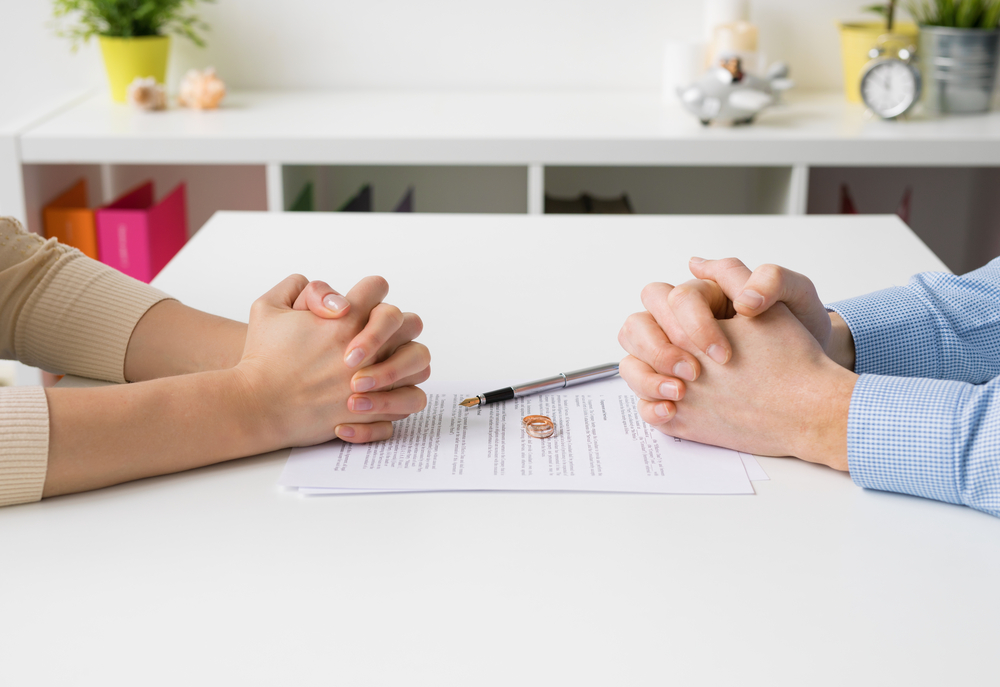 "Couple sitting across a desk, solemnly signing divorce papers, symbolizing the end of their marriage.