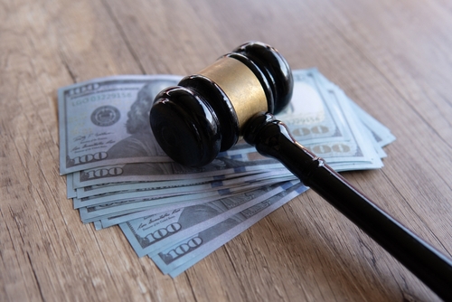 Close-up of a judge’s gavel resting on a stack of US hundred-dollar bills on a wooden table