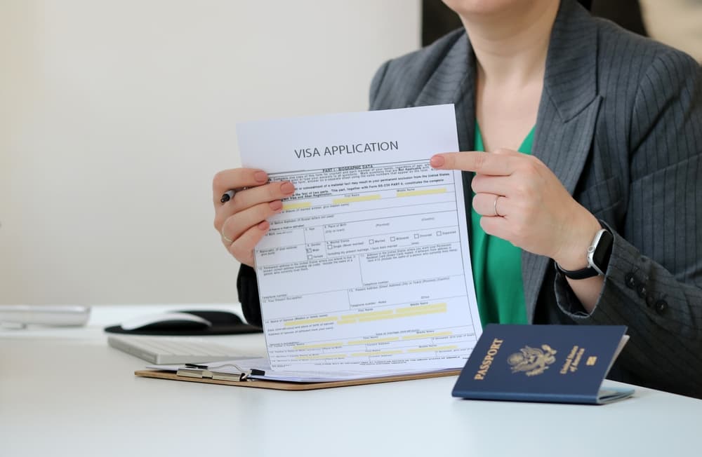 Woman holding a visa application paper document with an American passport laying on office table, visa document application 