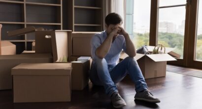 Tired unhappy bankrupt man moving out from apartment, sitting at pile of paper cardboard relocation boxes, waiting for delivery service, feeling headache, stress about eviction, divorce