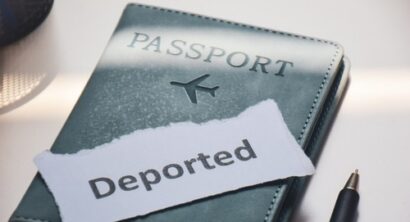 Travel passport with a torn paper reading “Deported” placed on top, representing deportation risk and immigration issues.