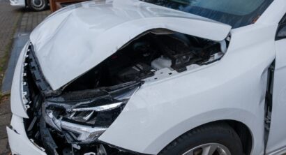 front of white crashed car close up, badly damaged car after car accident, huge dent in car body, reckless driving, insurance reminder.