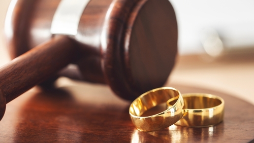 Two gold wedding bands placed beside a wooden judge’s gavel symbolizing a legal divorce proceeding.
