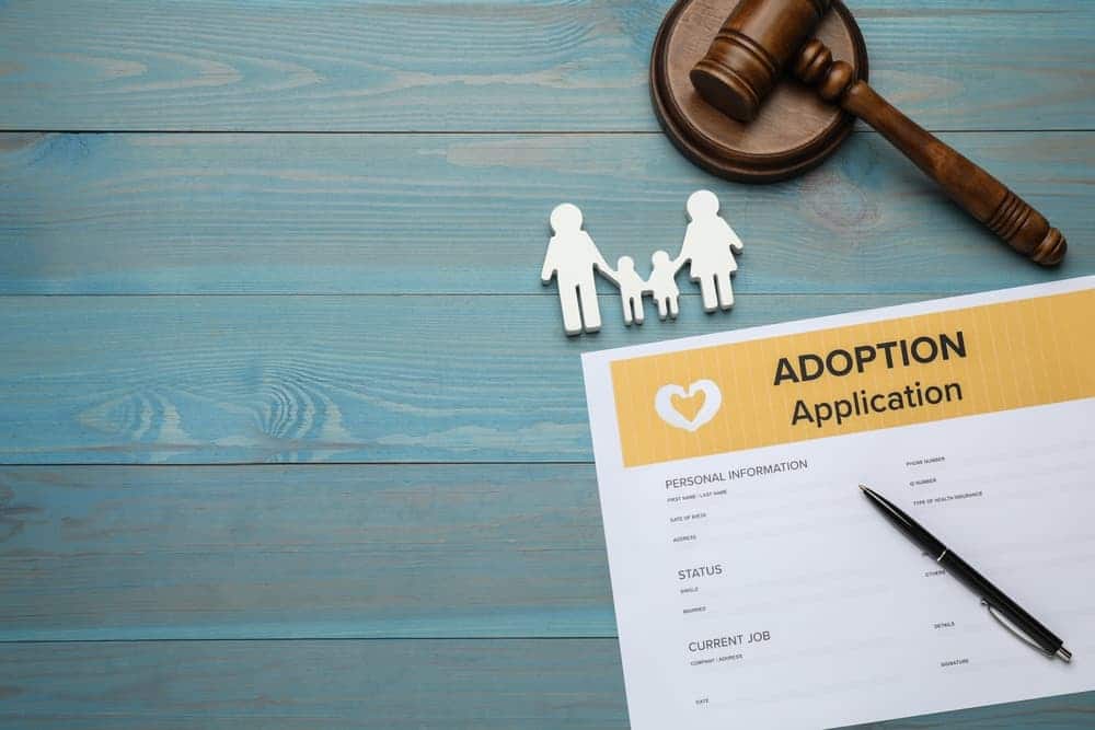 Adoption application, gavel, family figure and pen on blue wooden table,