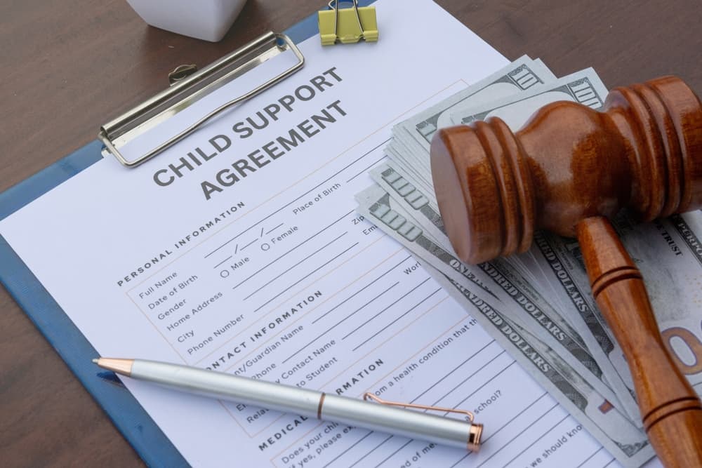 A detailed child support agreement paper on a desk with cash, a gavel, and a calculator, representing legal obligations and financial support.