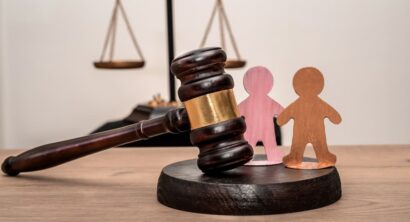 Judge's gavel, scales of justice, and two wooden figures symbolizing children, family law.