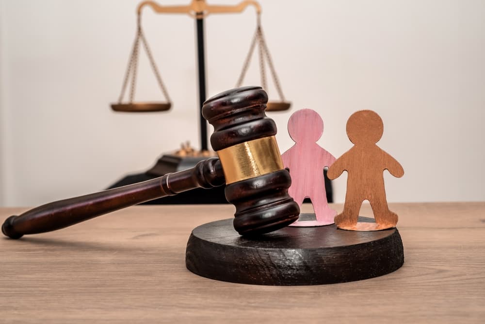 Judge's gavel, scales of justice, and two wooden figures symbolizing children, family law.