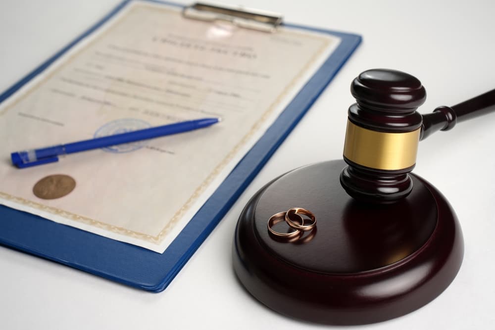 Judge gavel with wedding rings and a legal paper on table