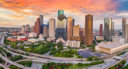 Houston skyline at sunset with downtown buildings and curving highways in the foreground.