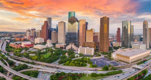 Houston skyline at sunset with downtown buildings and curving highways in the foreground.